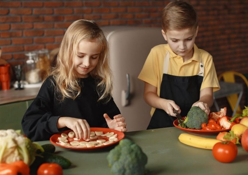 Two kids having fun preparing a healthy meal with fresh ingredients indoors.