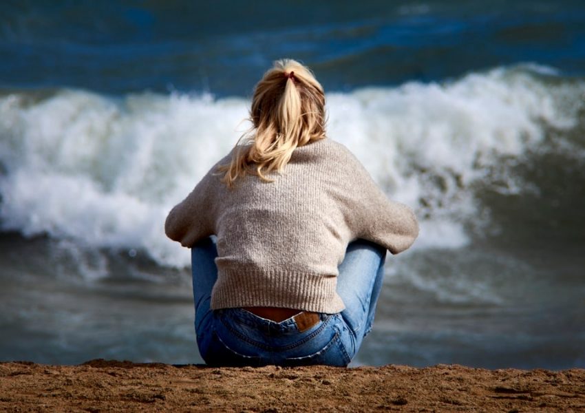 A woman sitting on a beach next to a body of water