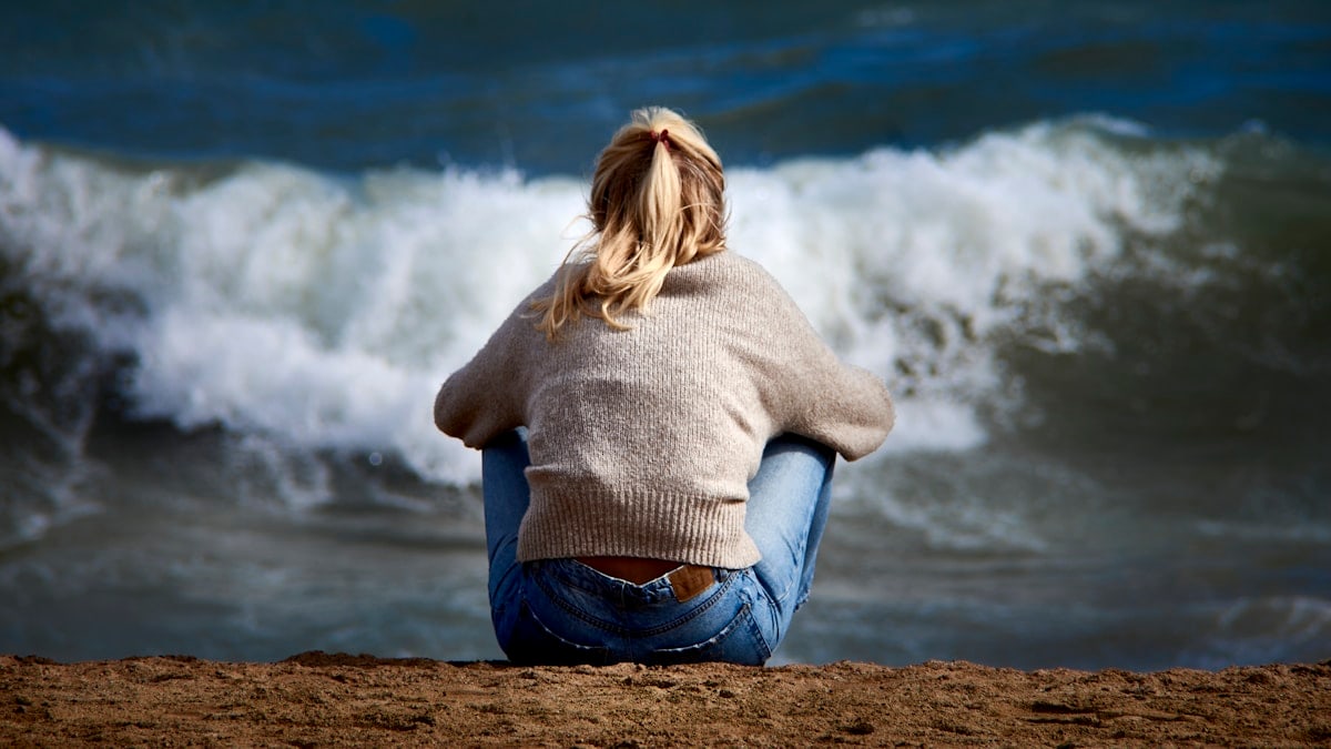 A woman sitting on a beach next to a body of water