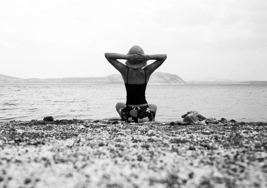 Back view of a woman sitting on a beach, gazing at the sea in black and white.