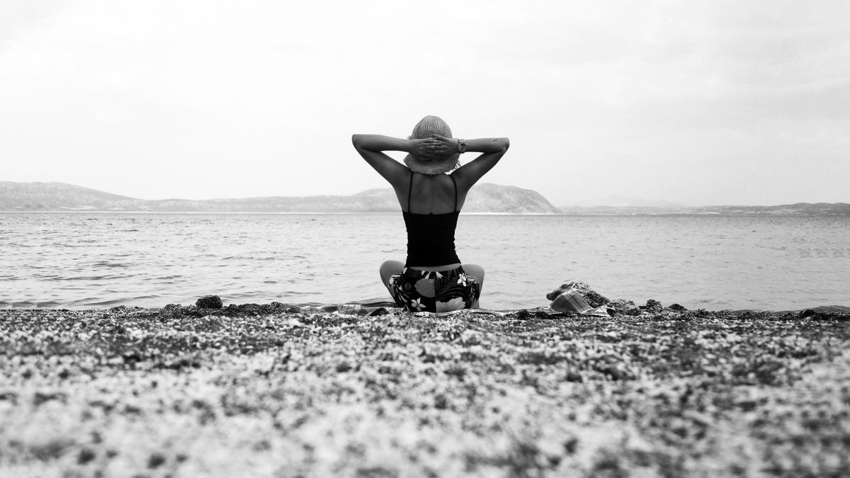 Back view of a woman sitting on a beach, gazing at the sea in black and white.